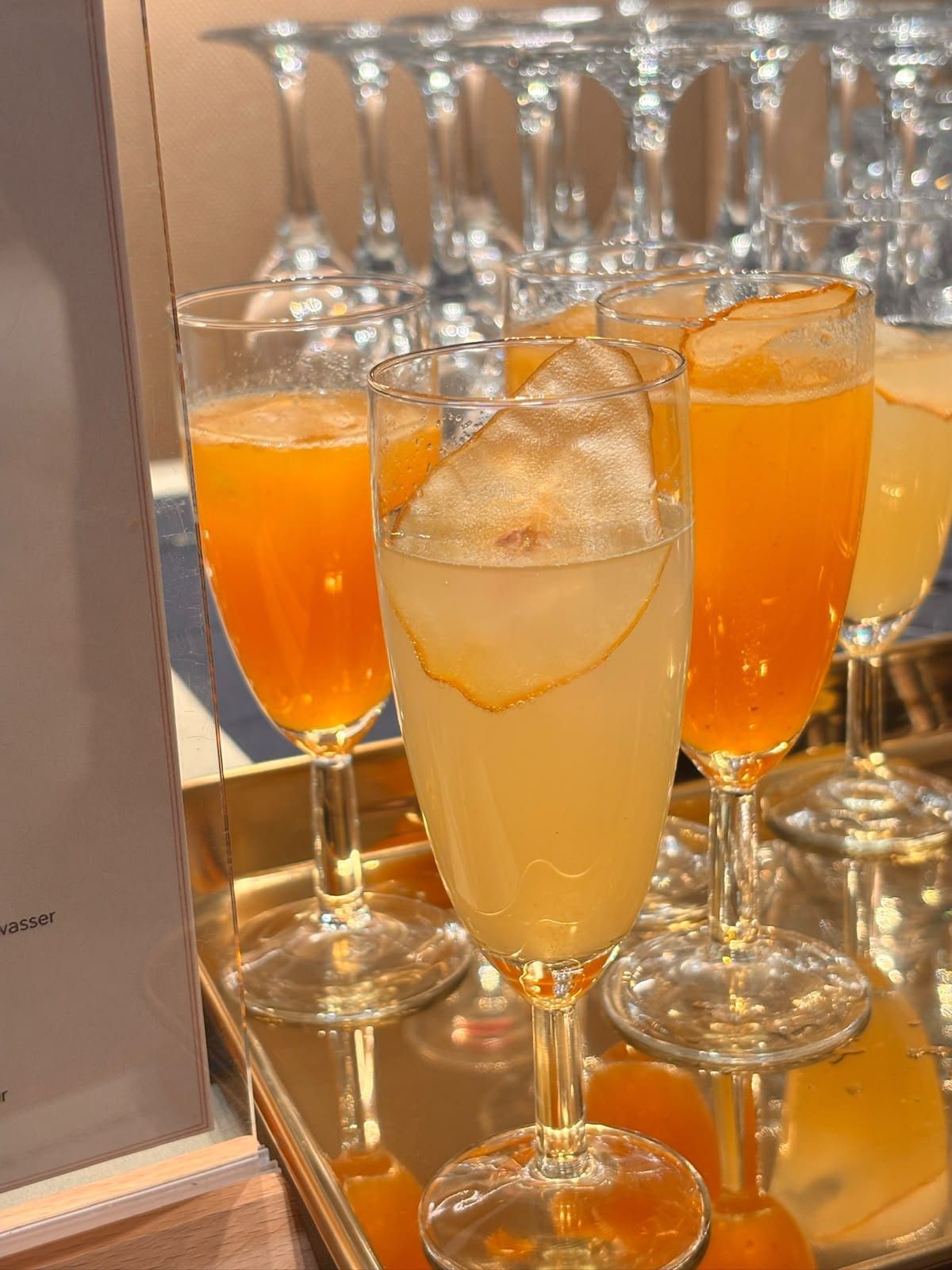 Sektflöten mit orangefarbenen und blassgelben Drinks und getrockneten Birnenscheiben auf einem goldenen Tablett