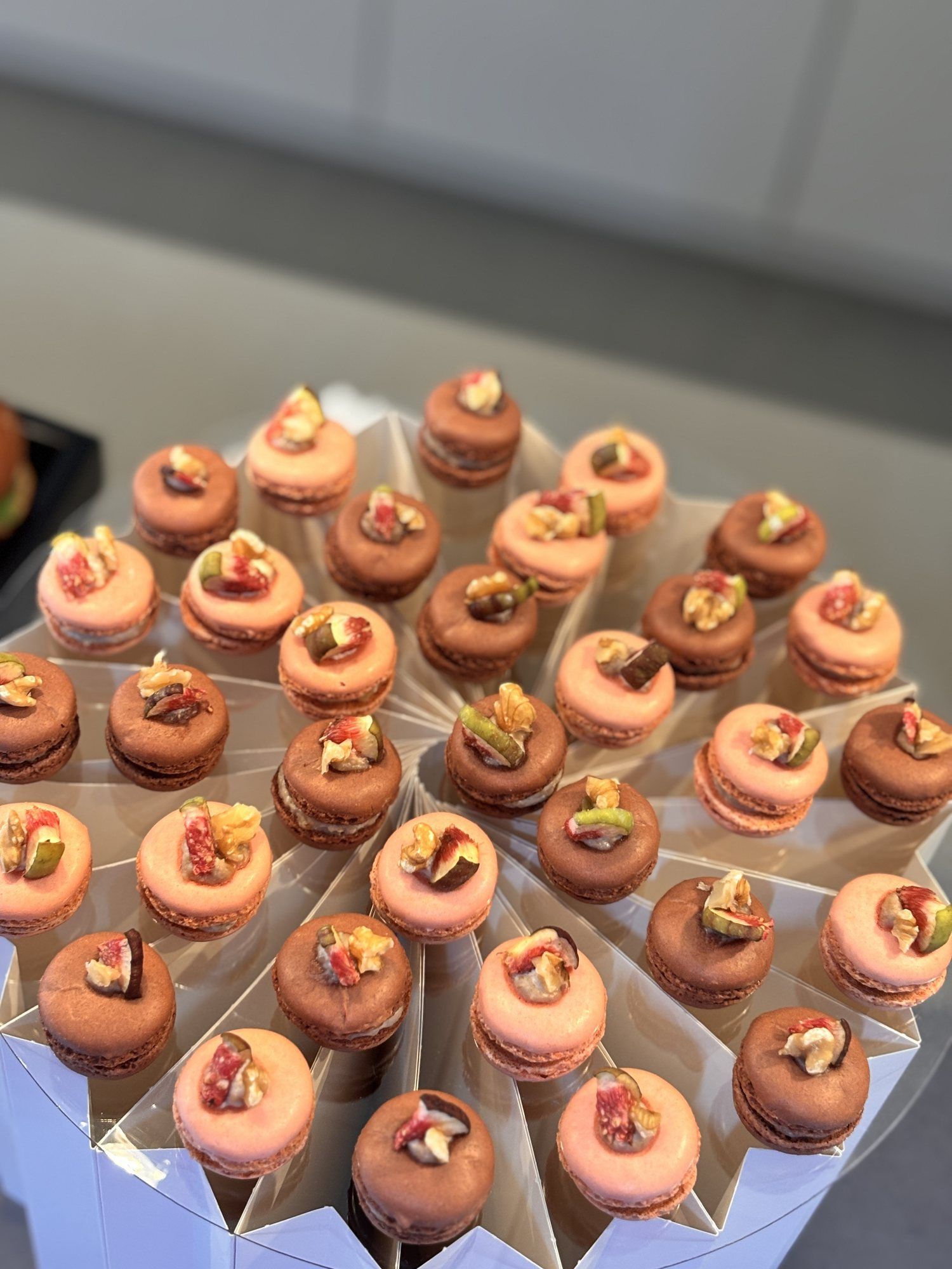 Macarons in Rosa und Braun, jeweils mit Feigenstücken belegt, kreisförmig auf einem Aufsteller angeordnet