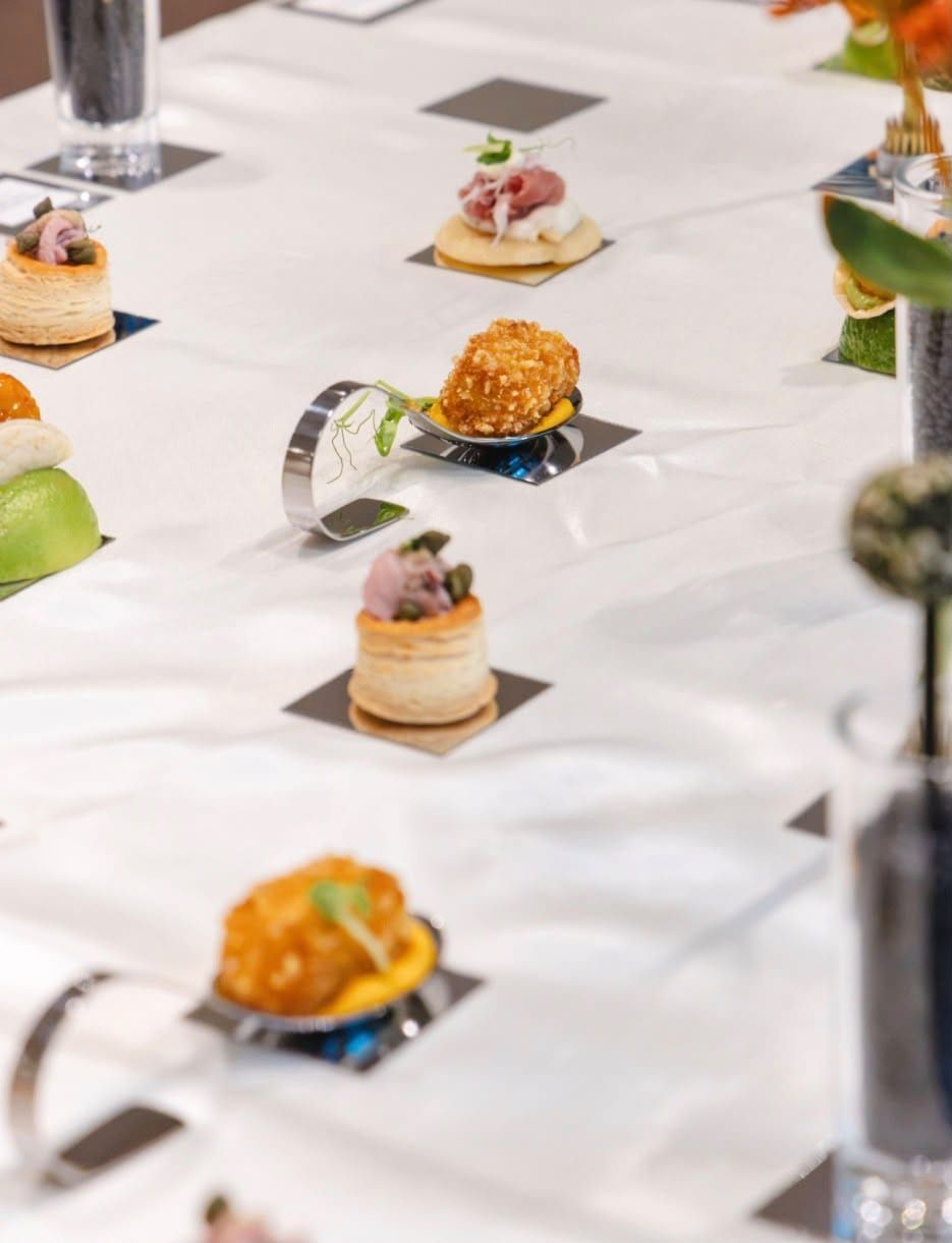 Einzelne Häppchen, darunter Blätterteigtörtchen, auf Spiegelplättchen in einer Reihe auf weißer Tafel