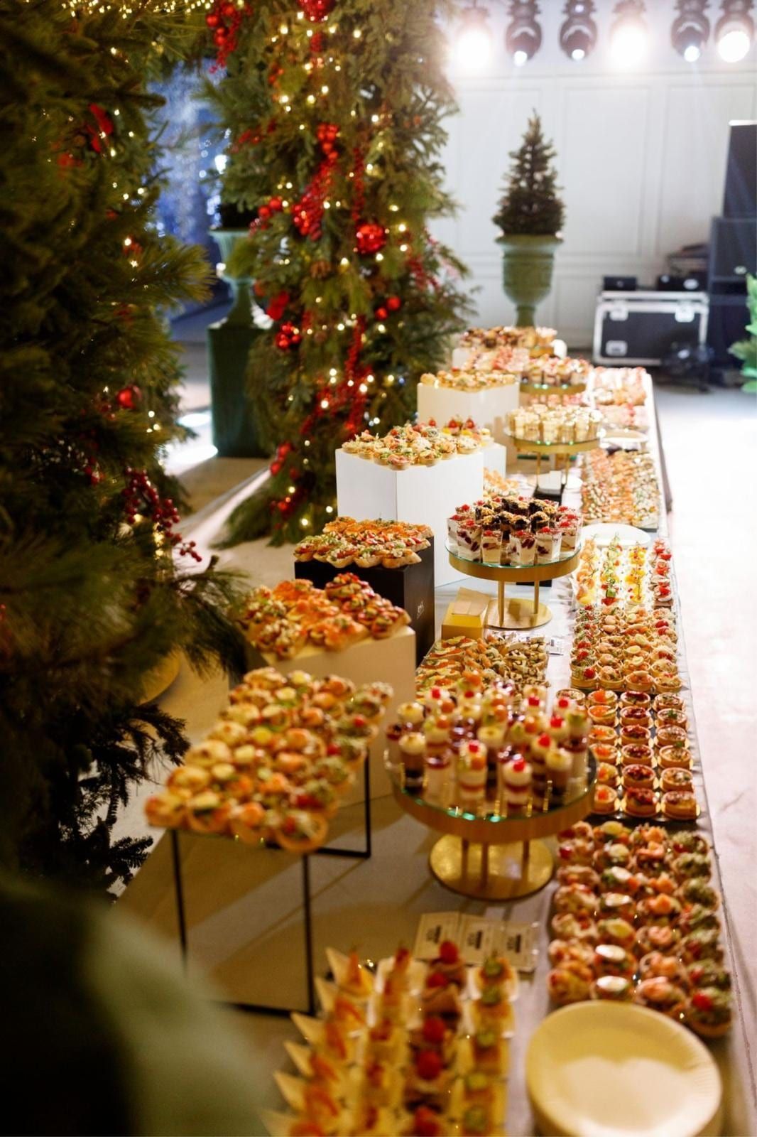 Lange Buffettafel mit Häppchen und Desserts neben geschmückten Weihnachtsbäumen